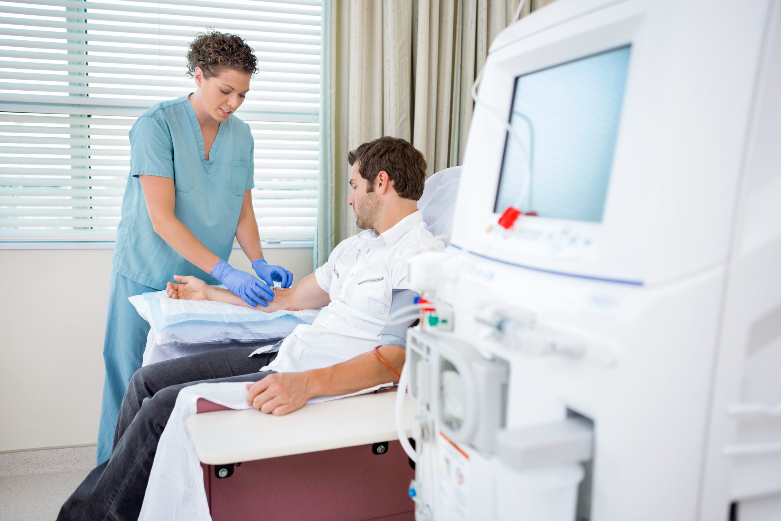 Mid adult female nurse injecting patient for renal dialysis treatment in hospital room
